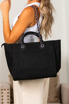 Black canvas tote bag with chain shoulder strap and structured shape, worn on shoulder
