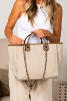 Bisque canvas tote bag with chain detail and zip top closure, handheld view
