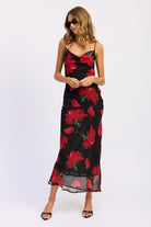 Model wearing a black floral slip dress with red flowers on a white background
