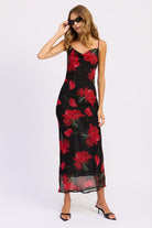 Model wearing a black dress with red floral patterns on a white background