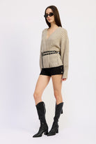 Full side view of model in warm grey ribbed knit wrap sweater with double grommet belt, black shorts and tall boots.
