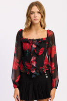 Model in black floral ruffle blouse with ruched bodice and long sleeves.