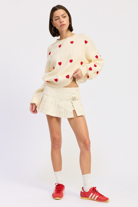 Ivory knit sweater with red heart details and textured pattern, styled with cream pleated mini skirt and red shoes