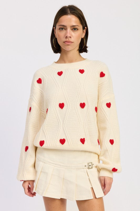 Ivory knit sweater with red heart details and textured pattern, styled with cream pleated mini skirt