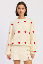 Ivory knit sweater with red heart details and textured pattern, styled with cream pleated mini skirt