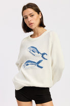 Front view of ivory knit sweater with blue fish graphic and long sleeves
