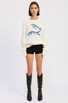 Full-length view of fish graphic knit sweater styled with black shorts and boots
