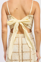 Close-up back view showing open-back bow tie on cream crochet mini dress.
