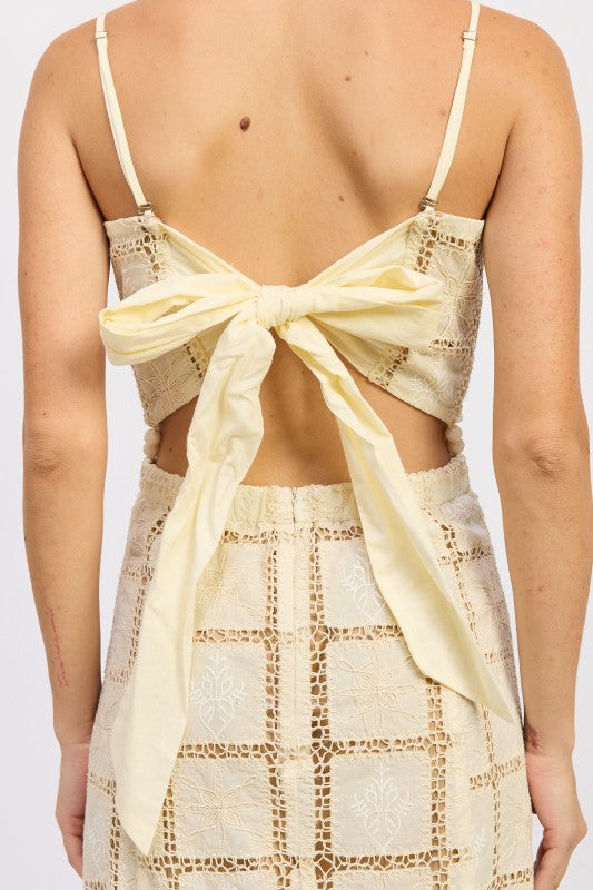 Close-up back view showing open-back bow tie on cream crochet mini dress.
