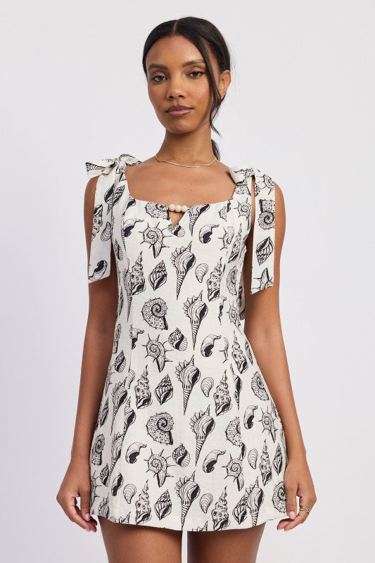 Model wearing a black-and-white seashell print mini dress with tie-shoulder straps and a bead keyhole detail - AVAH