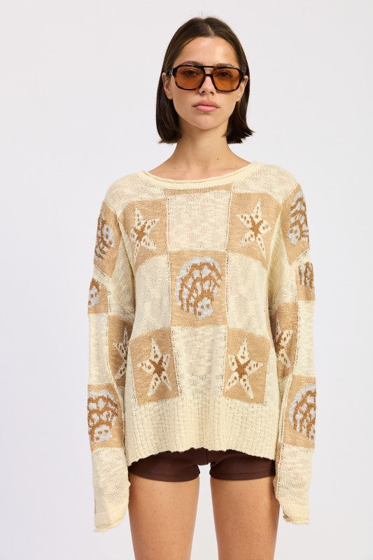 Model wearing cream and taupe patchwork knit sweater with star and seashell motifs, front view.