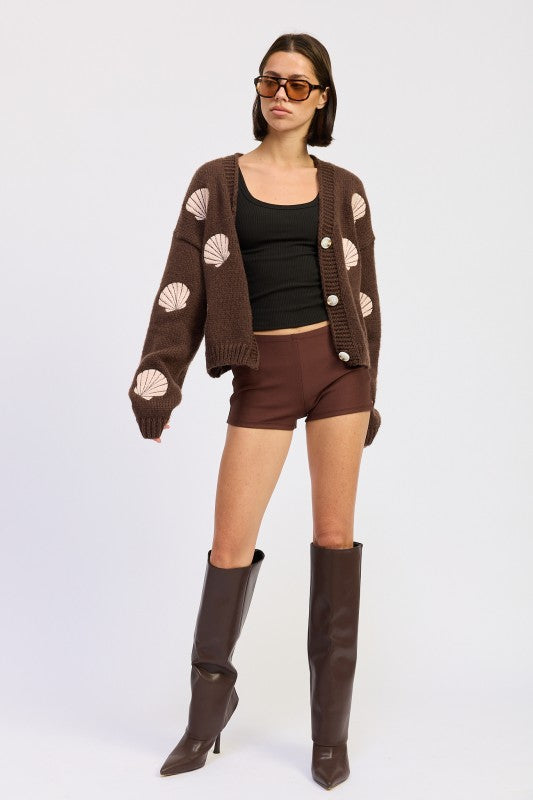 Full-body shot of model wearing mocha seashell cardigan with brown shorts and tall boots.