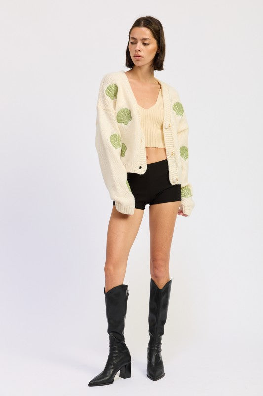 Model in ivory seashell cardigan facing forward in black shorts and knee-high boots.
