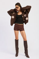 Full-body shot of model wearing mocha seashell cardigan with brown shorts and tall boots.