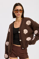 Model wearing mocha seashell cardigan with pink embroidered shells, front view with V-neck and oversized sleeves.