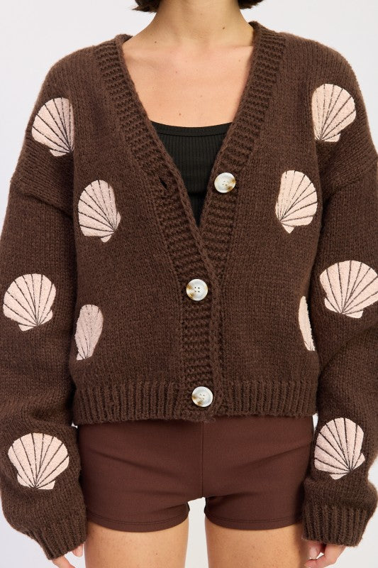 Close-up of mocha knit cardigan showing pink seashell embroidery and button details.
