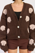 Close-up of mocha knit cardigan showing pink seashell embroidery and button details.
