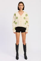 Model in ivory seashell cardigan facing forward in black shorts and knee-high boots.
