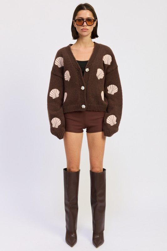Full-body shot of model wearing mocha seashell cardigan with brown shorts and tall boots.