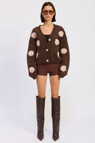 Full-body shot of model wearing mocha seashell cardigan with brown shorts and tall boots.