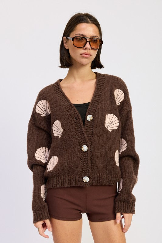 Model wearing mocha seashell cardigan with pink embroidered shells, front view with V-neck and oversized sleeves.