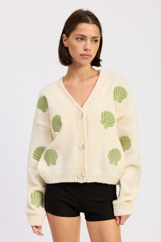 Model wearing ivory seashell cardigan with green embroidered shells, front view with oversized fit.
