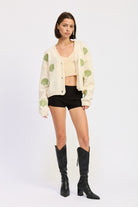 Model in ivory seashell cardigan facing forward in black shorts and knee-high boots.
