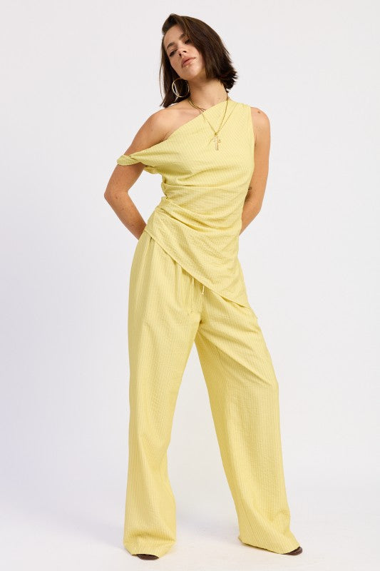 Woman wearing a pale yellow one shoulder asymmetrical top with black stripe against a white background