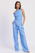 Woman wearing a blue one shoulder asymmetrical top with black stripe against a white background