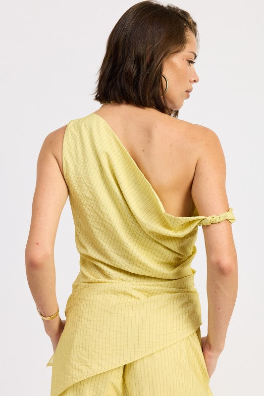 Woman wearing a pale yellow one shoulder asymmetrical top with black stripe against a white background