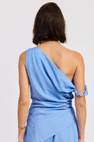 Woman wearing a blue one shoulder asymmetrical top with black stripe against a white background
