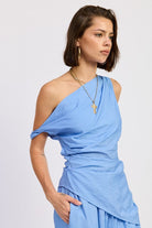 Woman wearing a blue one shoulder asymmetrical top with black stripe against a white background
