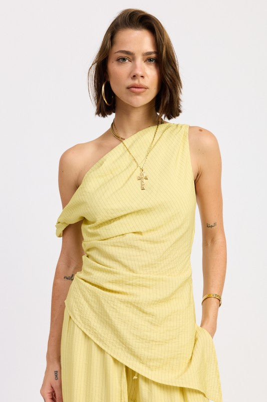 Woman wearing a pale yellow one shoulder asymmetrical top with black stripe against a white background