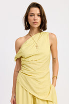Woman wearing a pale yellow one shoulder asymmetrical top with black stripe against a white background