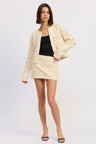 Model wearing Ivory Reverie Textured Cropped Jacket and matching mini skirt, styled with black tank top.