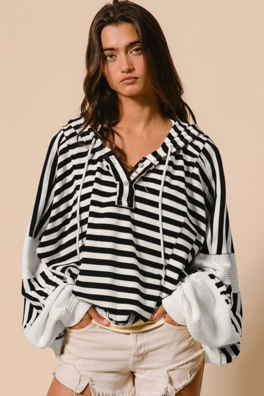 Black and white striped hooded pullover top with relaxed fit and button placket neckline, styled with distressed denim shorts