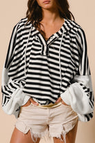 Close-up of striped hooded knit top showing button placket neckline, drawstrings, and contrast sleeve texture