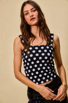 model wearing a black ribbed tank top with white polka dots, featuring a square neckline, wide straps, and a fitted silhouette.