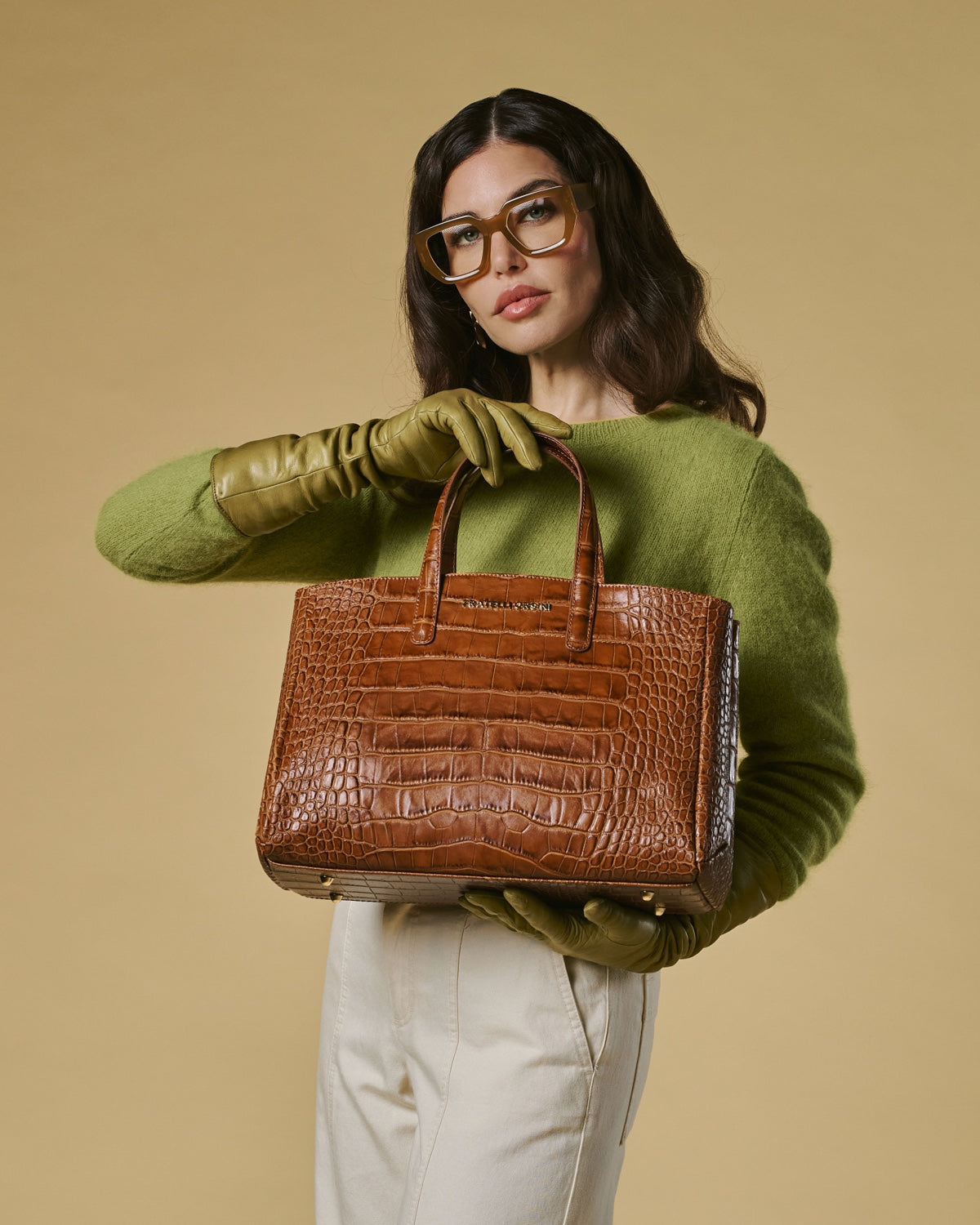 Woman holding a brown crocodile-patterned handbag against a beige background