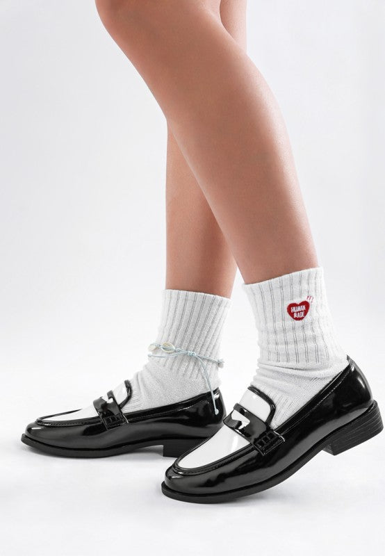 Side view of black patent leather shoes worn with white socks on a light gray background