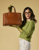 Woman holding a brown crocodile skin handbag against a beige background