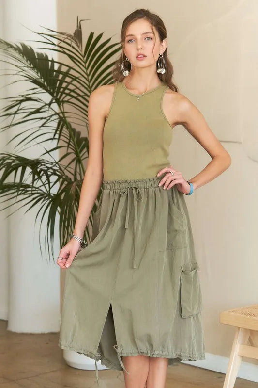 Model wearing an olive green mixed media cargo midi dress with a ribbed tank bodice, cargo pockets, drawstring waist, and adjustable drawstring hem.