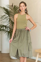 Model wearing an olive green mixed media cargo midi dress with a ribbed tank bodice, cargo pockets, drawstring waist, and adjustable drawstring hem.