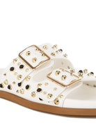 Close-up of white double buckle sandal with metallic studs on faux leather