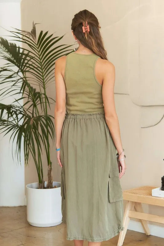Model wearing an olive green mixed media cargo midi dress with a ribbed tank bodice, cargo pockets, drawstring waist, and adjustable drawstring hem.