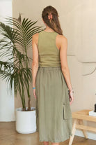 Model wearing an olive green mixed media cargo midi dress with a ribbed tank bodice, cargo pockets, drawstring waist, and adjustable drawstring hem.
