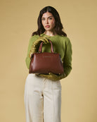 Woman holding a brown handbag against a beige background