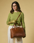 Woman in green sweater holding a brown handbag against a beige background