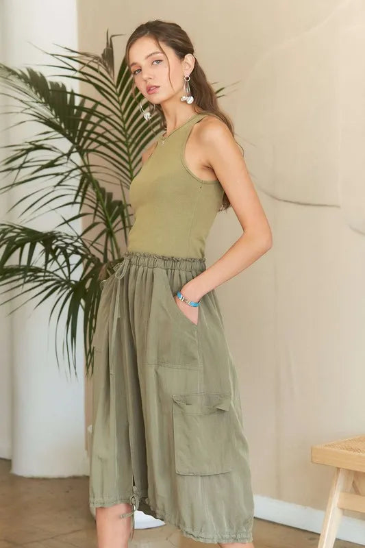 Model wearing an olive green mixed media cargo midi dress with a ribbed tank bodice, cargo pockets, drawstring waist, and adjustable drawstring hem.