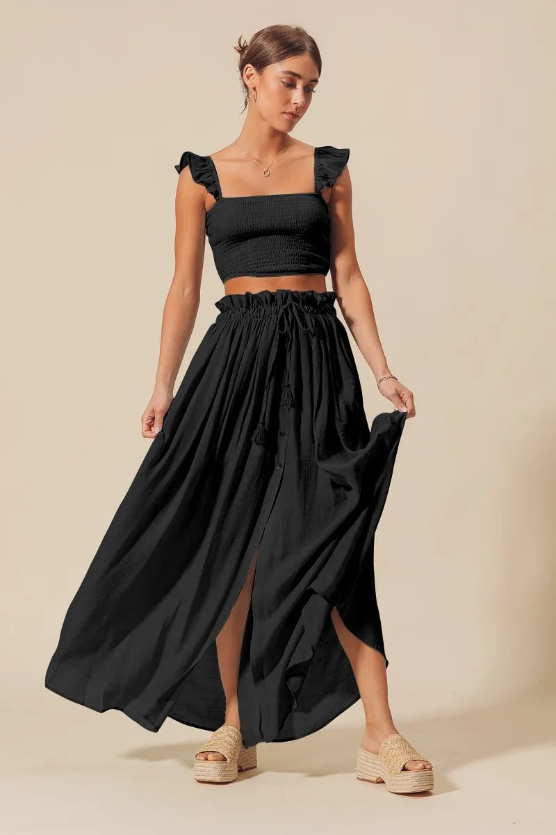 Woman wearing black smocked crop top and flowy maxi skirt set with slit

